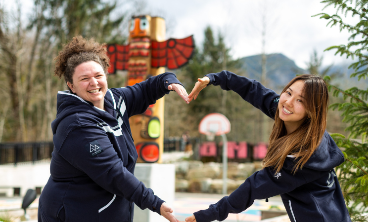 Two Foundry Staff make the shape of a heart in front of the Welcome Totem at Foundry Sea to Sky